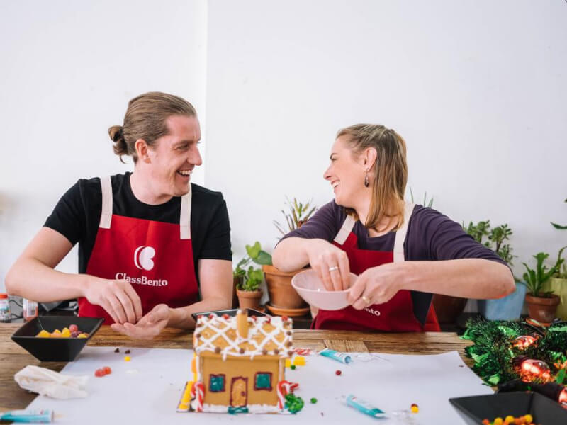 Two people laughing as they make a gingerbread house together